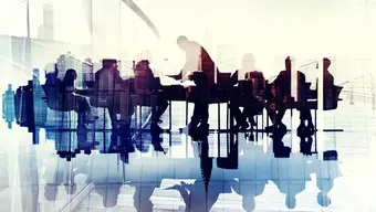 Grafika ilustracyjna przedstawiająca sylwetki ludzi siedzących przy stole i uczestniczących w spotkaniu