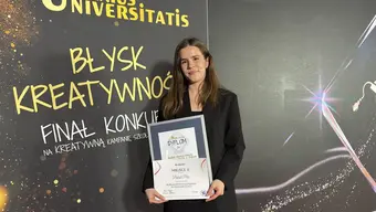 Osoba na zdjęciu trzyma w rękach pamiątkowy dyplom. W tle widać ściankę z kolorową grafiką i napisami "Genius Universitatis", "Błysk kreatywności" oraz "Finał konkursu na kreatywną kampanię szkoły wyższej"