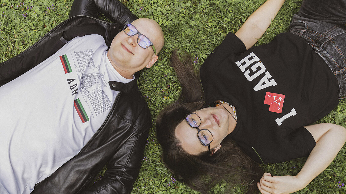 Meżczyzna i kobieta w koszulkach z logo AGH leżą na trawie 